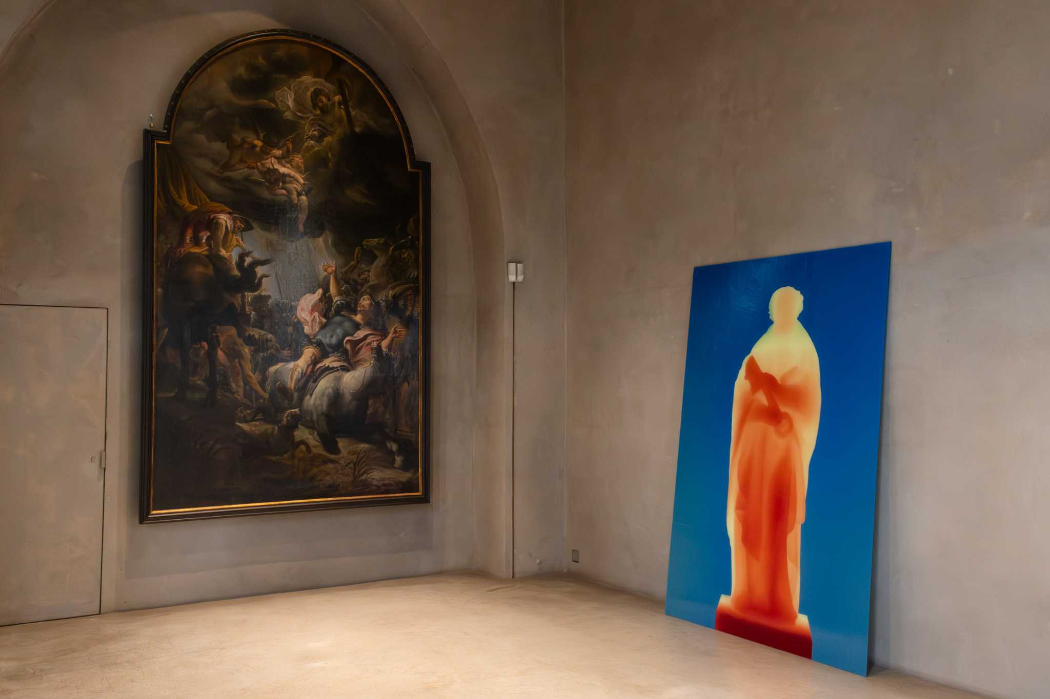 The print leaning in the corner of a room, a large baroque altar painting hanging on the wall to the left.