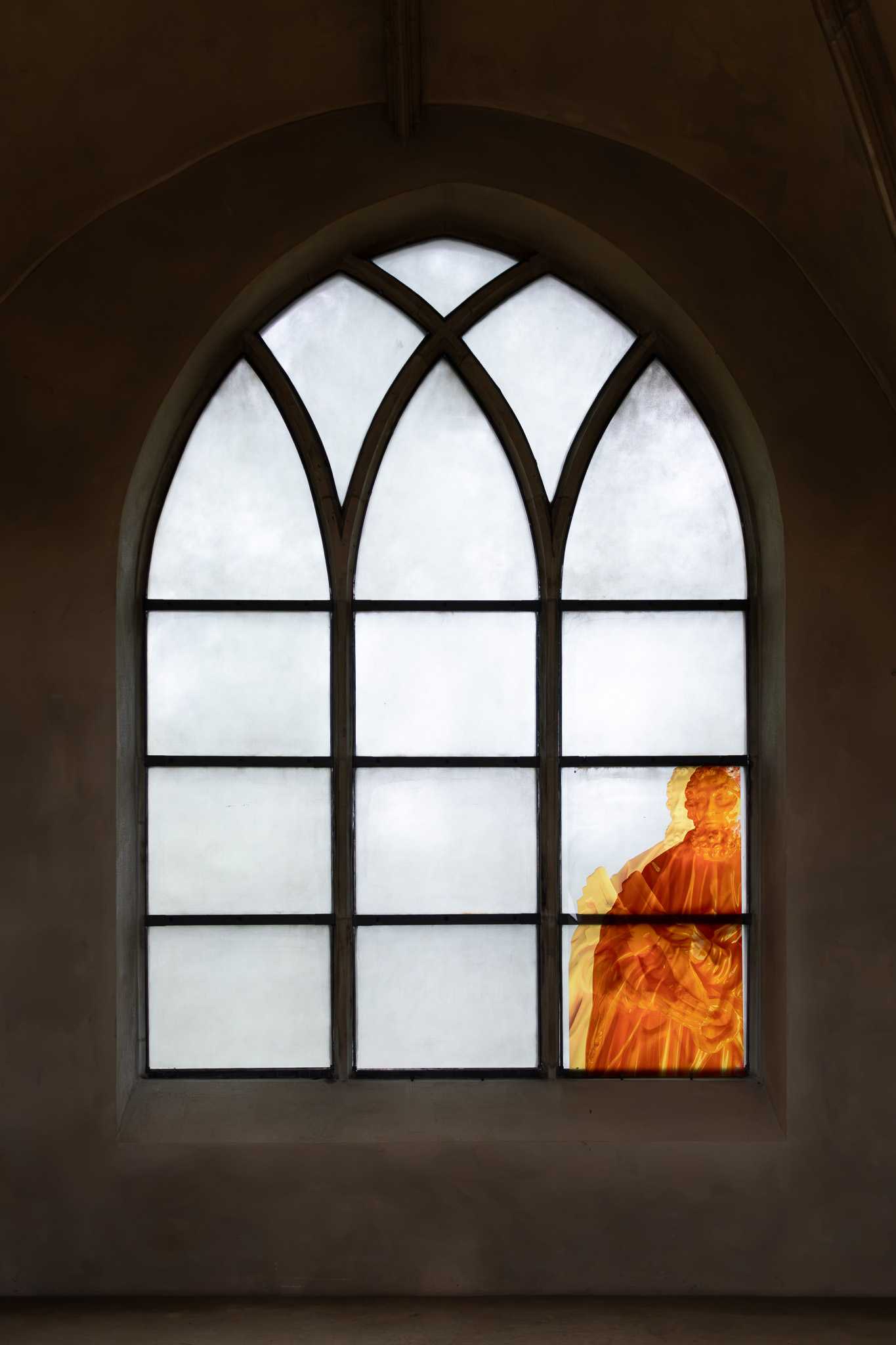 A deep-set pointed-arch window of three white glazed lights; a translucent orange print of Saint Peter with his key fills the lower panels of the right-hand light.