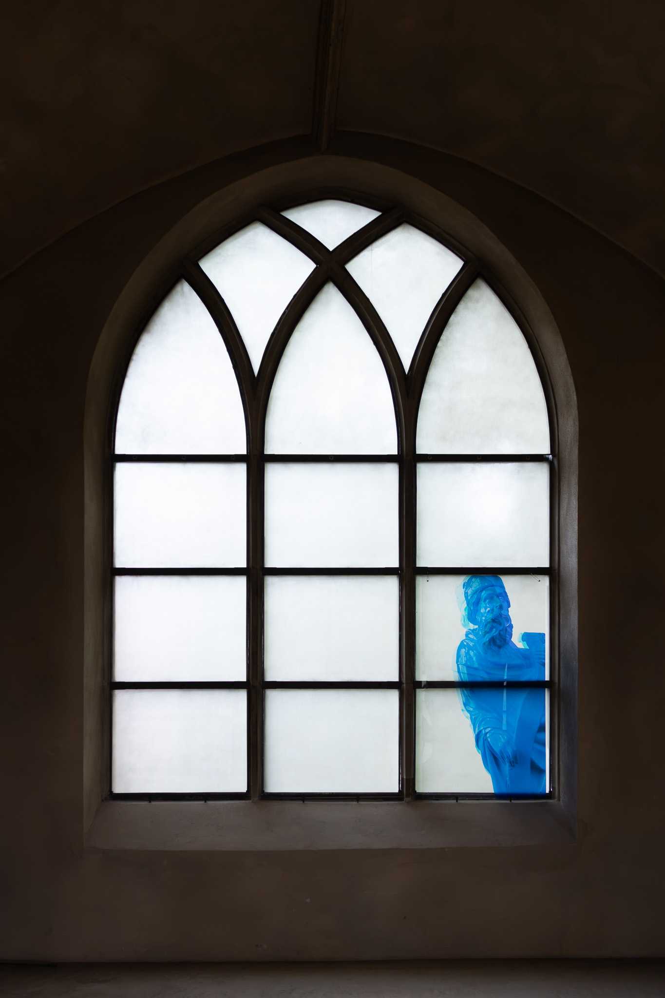 A deep-set pointed-arch window of three white glazed lights; a translucent blue print of the prophet with his scroll fills the lower panels of the right-hand light.